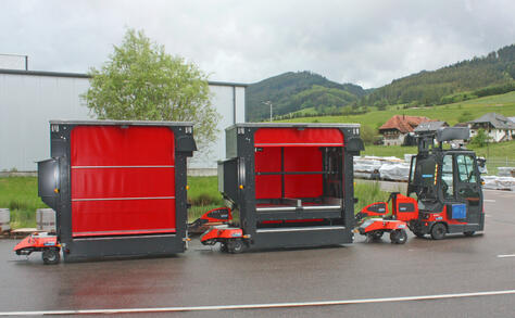 Fully automated and autonomous Factory Train outdoor tugger train from Neumaier Industry with roller conveyor load carrier for automated loading of stationary conveyor technology or unloading on stationary conveyor technology.